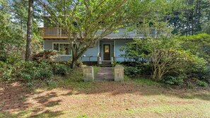 A two-story house with a front porch, surrounded by dense vegetation. - Wooded Lakefront Retreat (Port Orford)