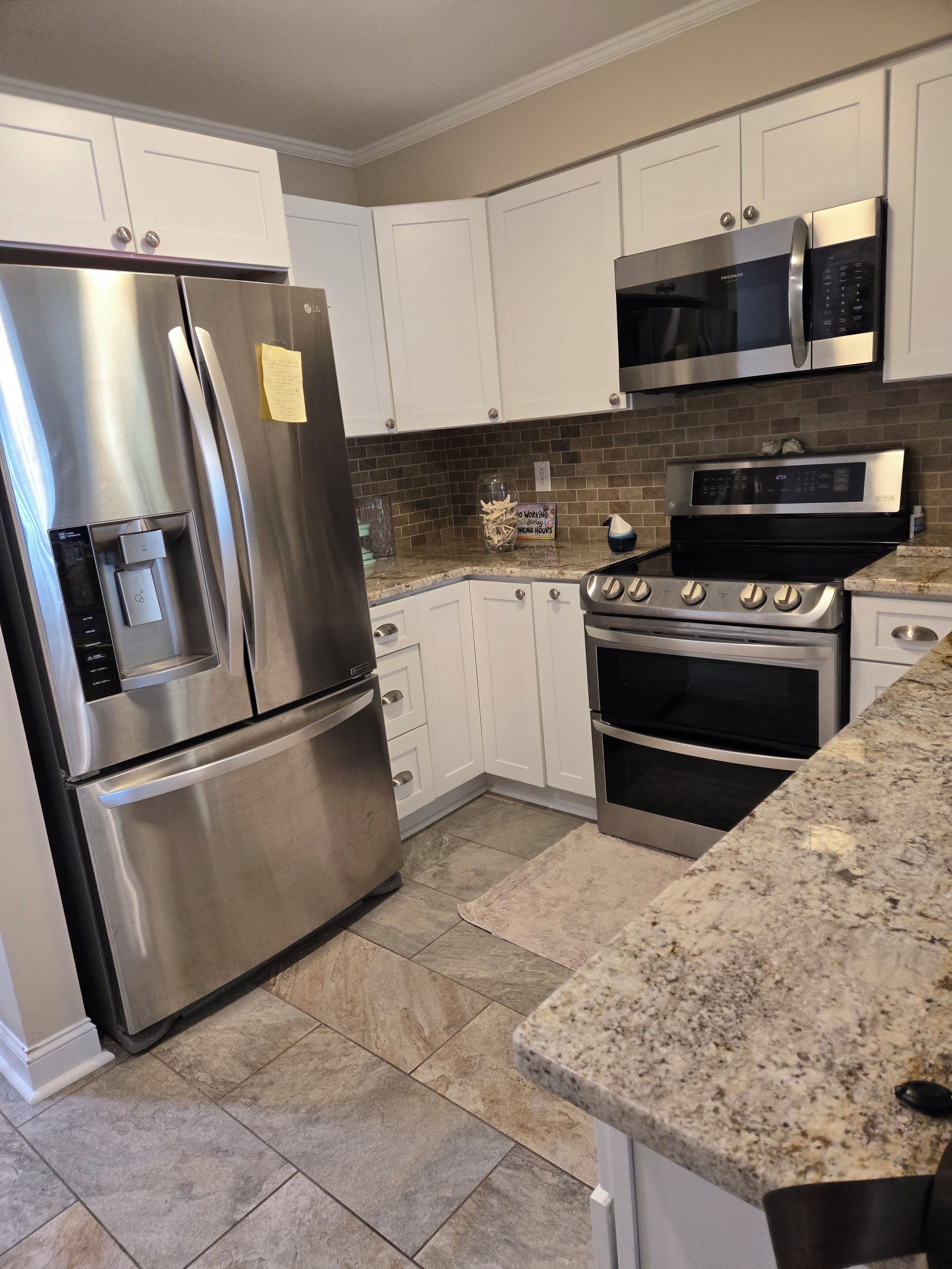 A modern kitchen with stainless steel appliances, white cabinets, and a granite countertop.