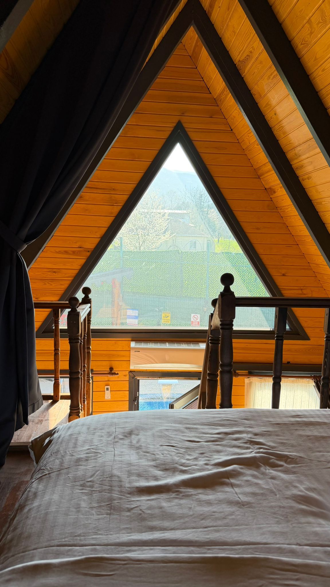 A bedroom with a sloped ceiling and a view of a green landscape through a window.