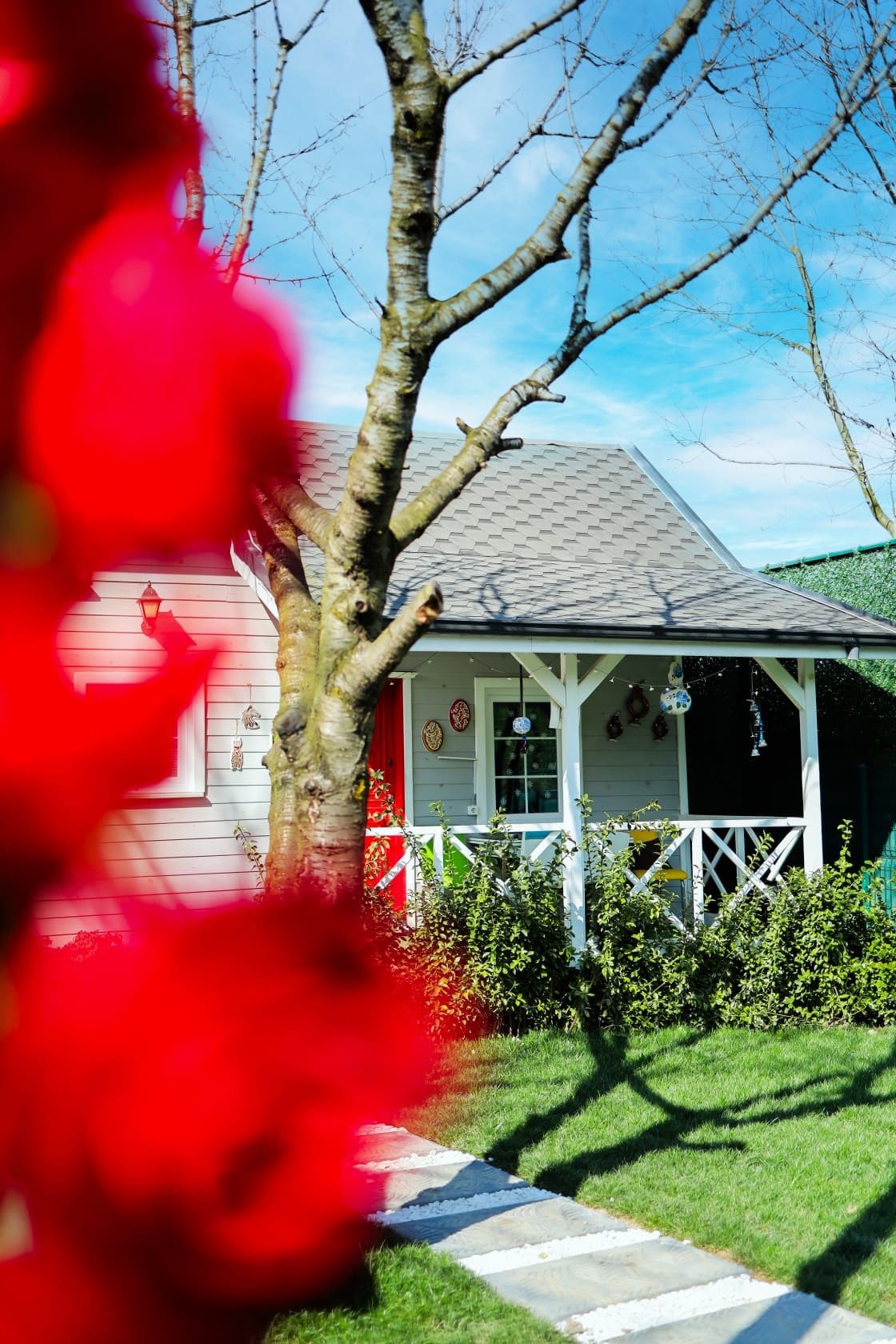 Una casa con porche, un árbol en primer plano y un cielo despejado.