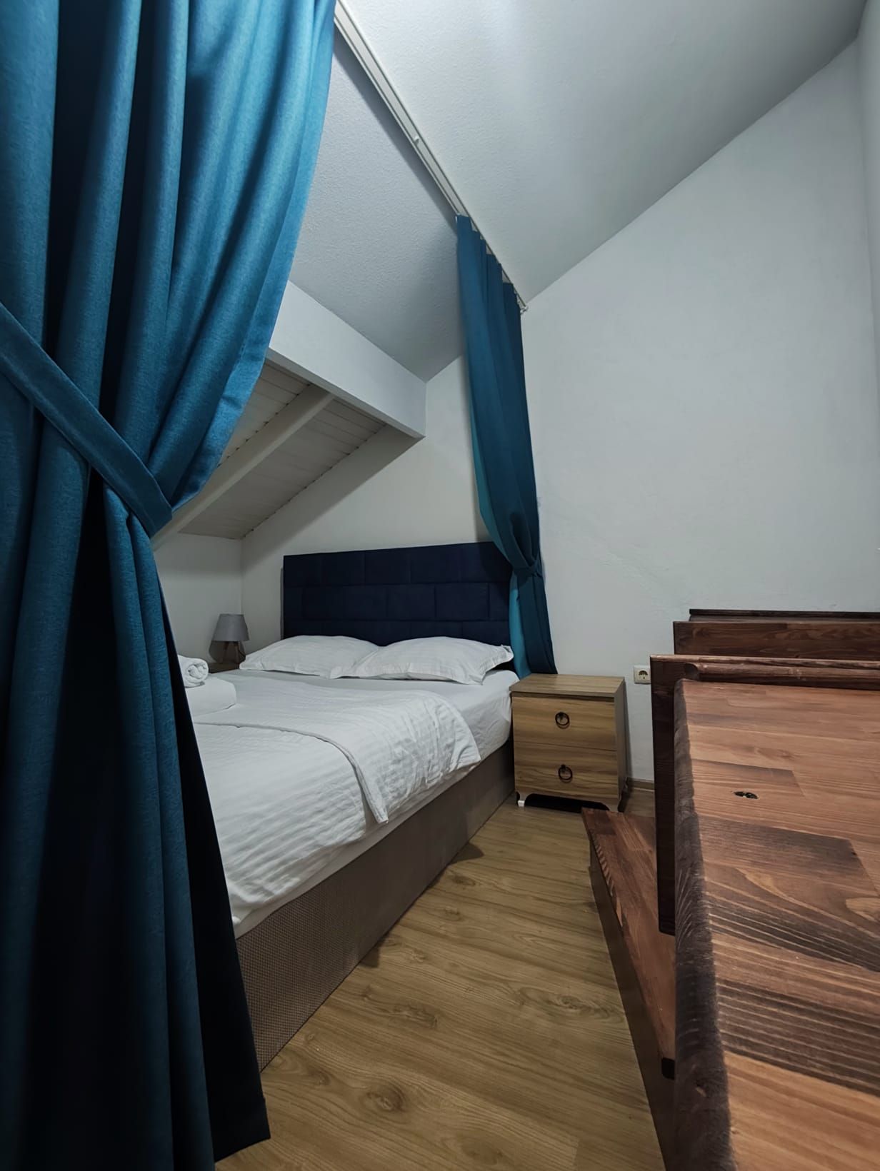 Un dormitorio con una cama, una mesita de noche, un aparador de madera y cortinas azules.