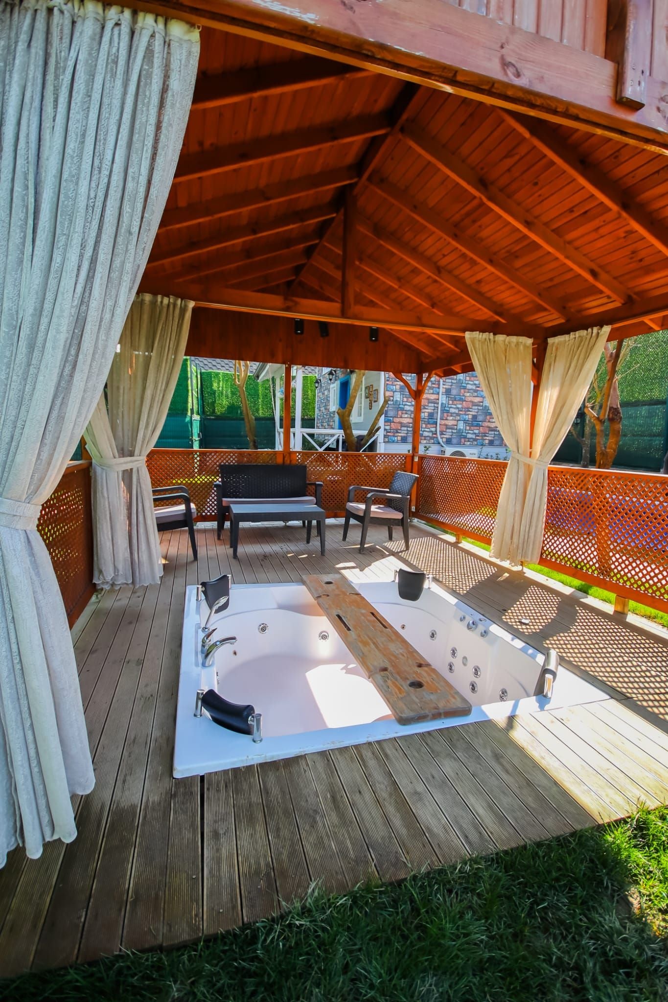A wooden deck with a hot tub, outdoor seating, and a covered area with curtains.
