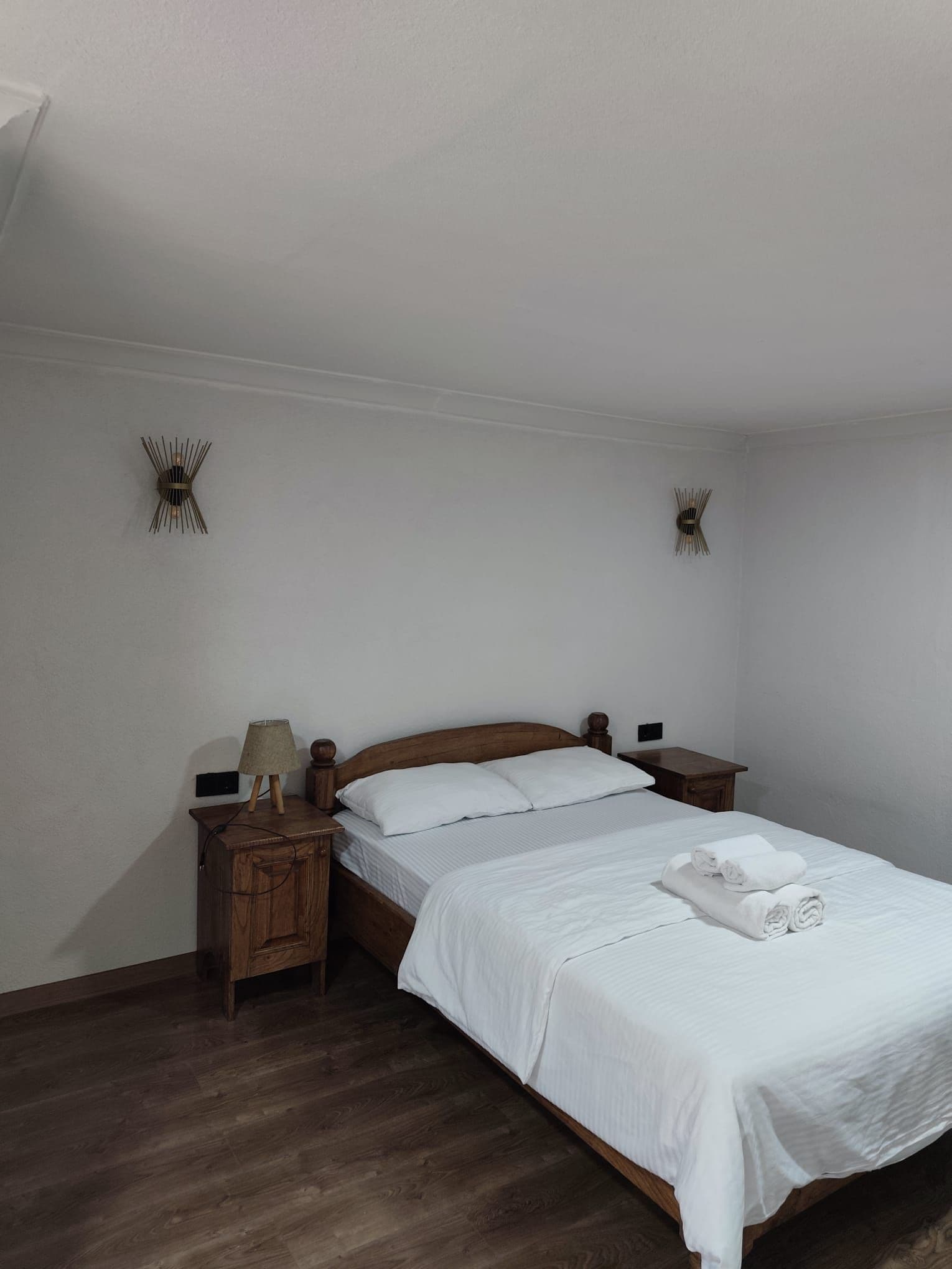Camera da letto con un letto in legno, biancheria bianca, un comodino con una lampada e due luci a parete.