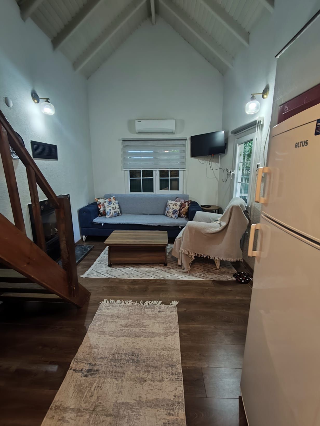 A compact living space with a sofa, a small table, a refrigerator, and a staircase.