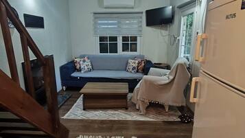 A compact living space with a sofa, a small table, a refrigerator, and a staircase.