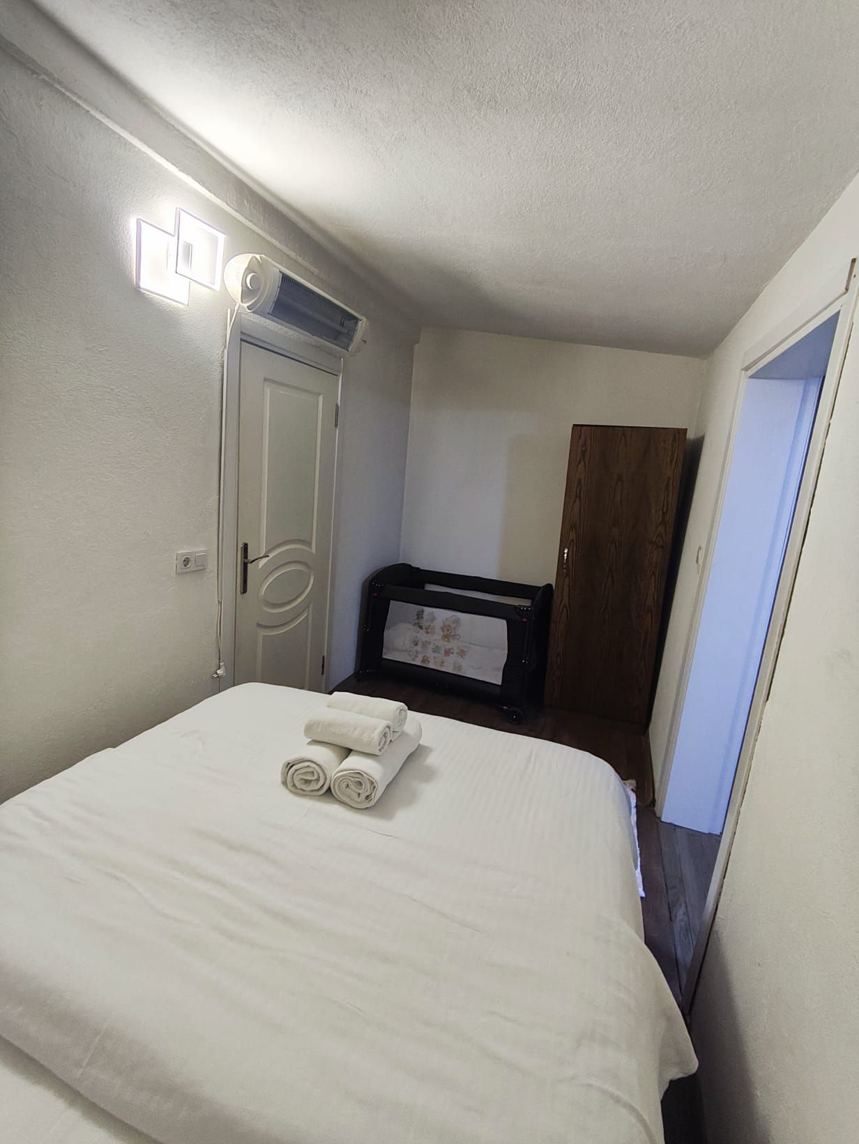 A hotel room with a bed, a wardrobe, a desk with a chair, and a mirror.