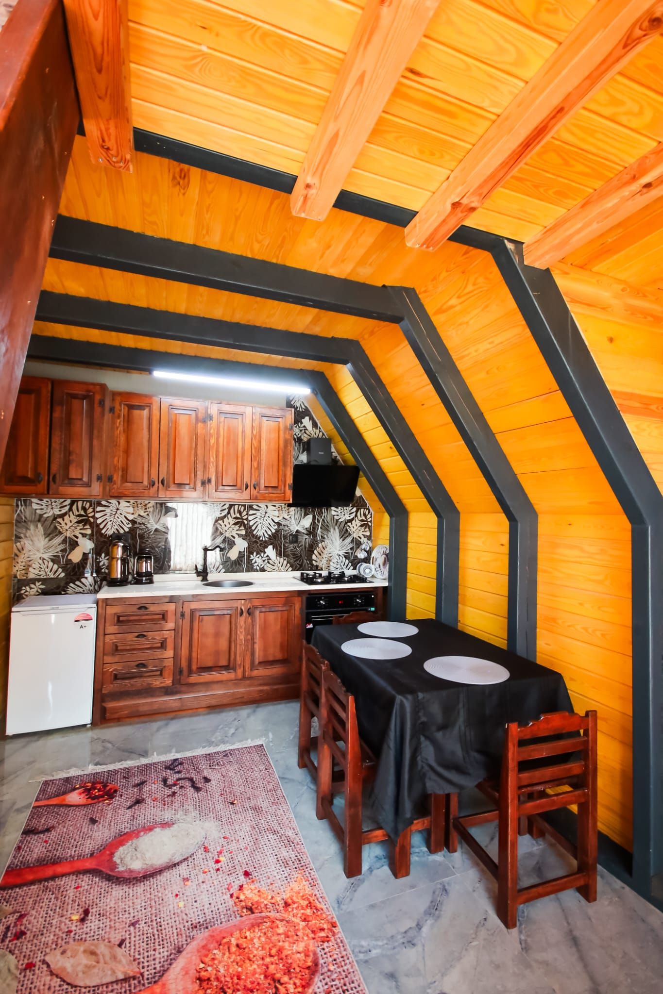 An attic kitchen with wooden cabinets, a stove, and a dining table set for two.