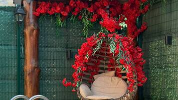 A swimming pool with a waterfall feature, a hanging chair, and red flowers.