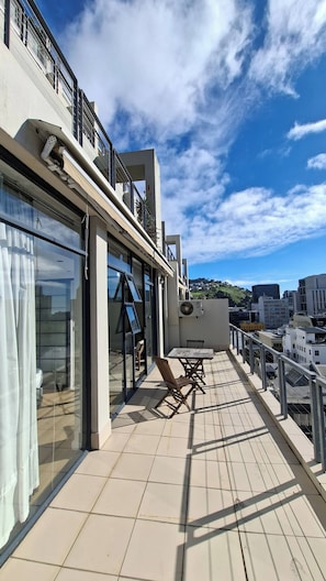 Une terrasse sur le toit avec un mur de verre, des sièges extérieurs et une vue sur le paysage urbain.
