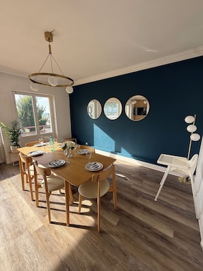 Un'area pranzo con tavolo in legno apparecchiato per quattro persone, una parete d'accento blu e tre specchi rotondi.