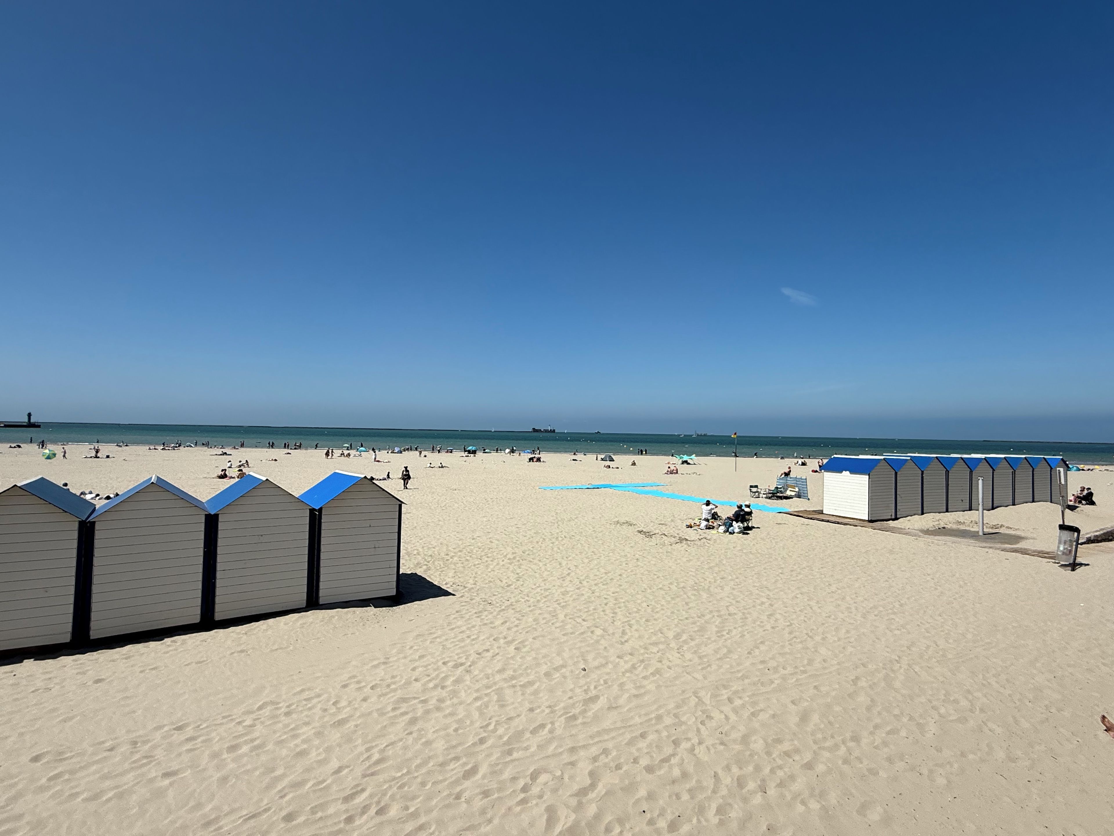 A beach with sand, a clear sky, and a row of beach huts.