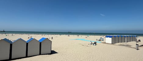 A beach with sand, a clear sky, and a row of beach huts.