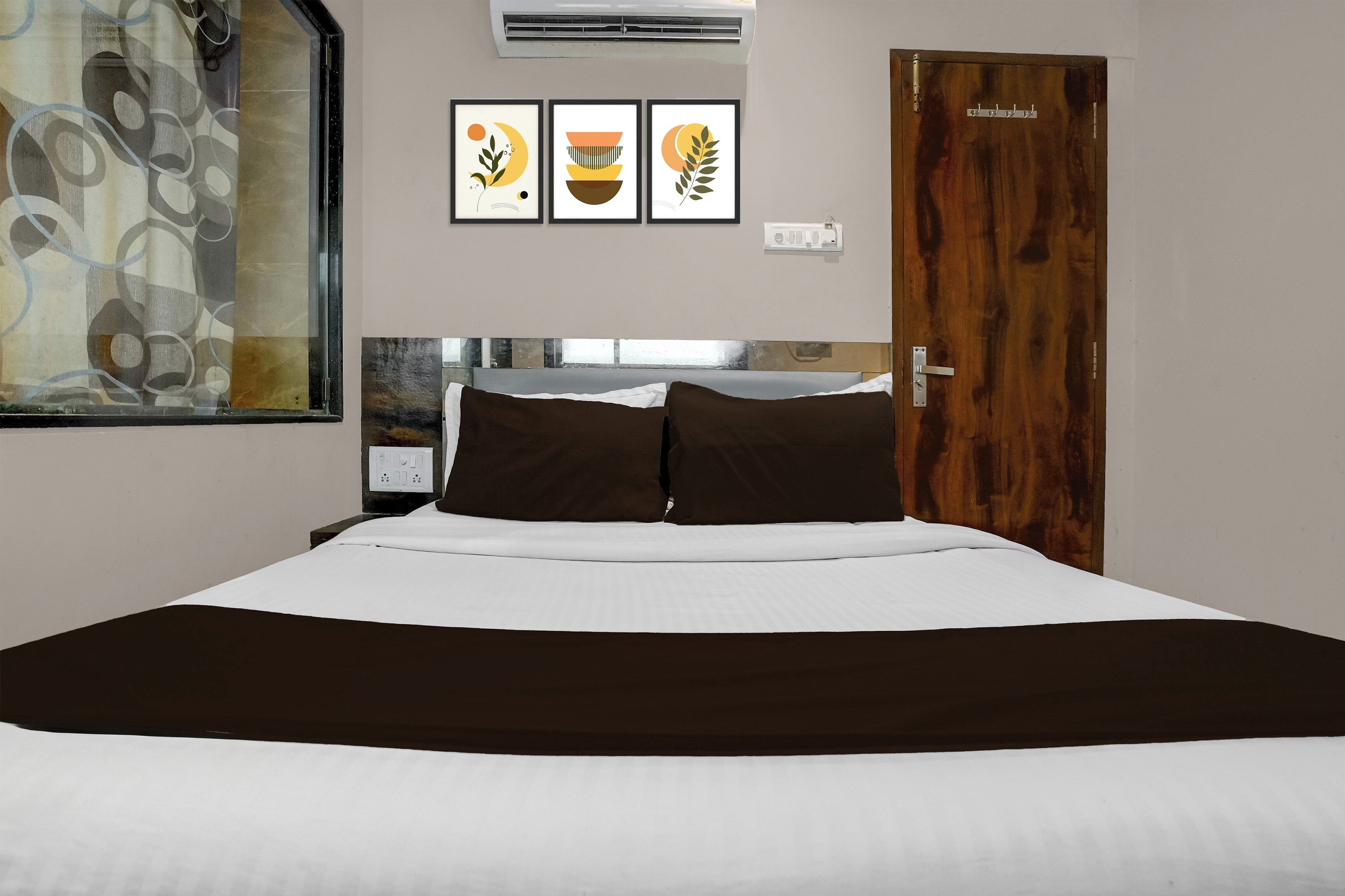 Habitación de hotel con una cama, una puerta de madera y tres cuadros en la pared.