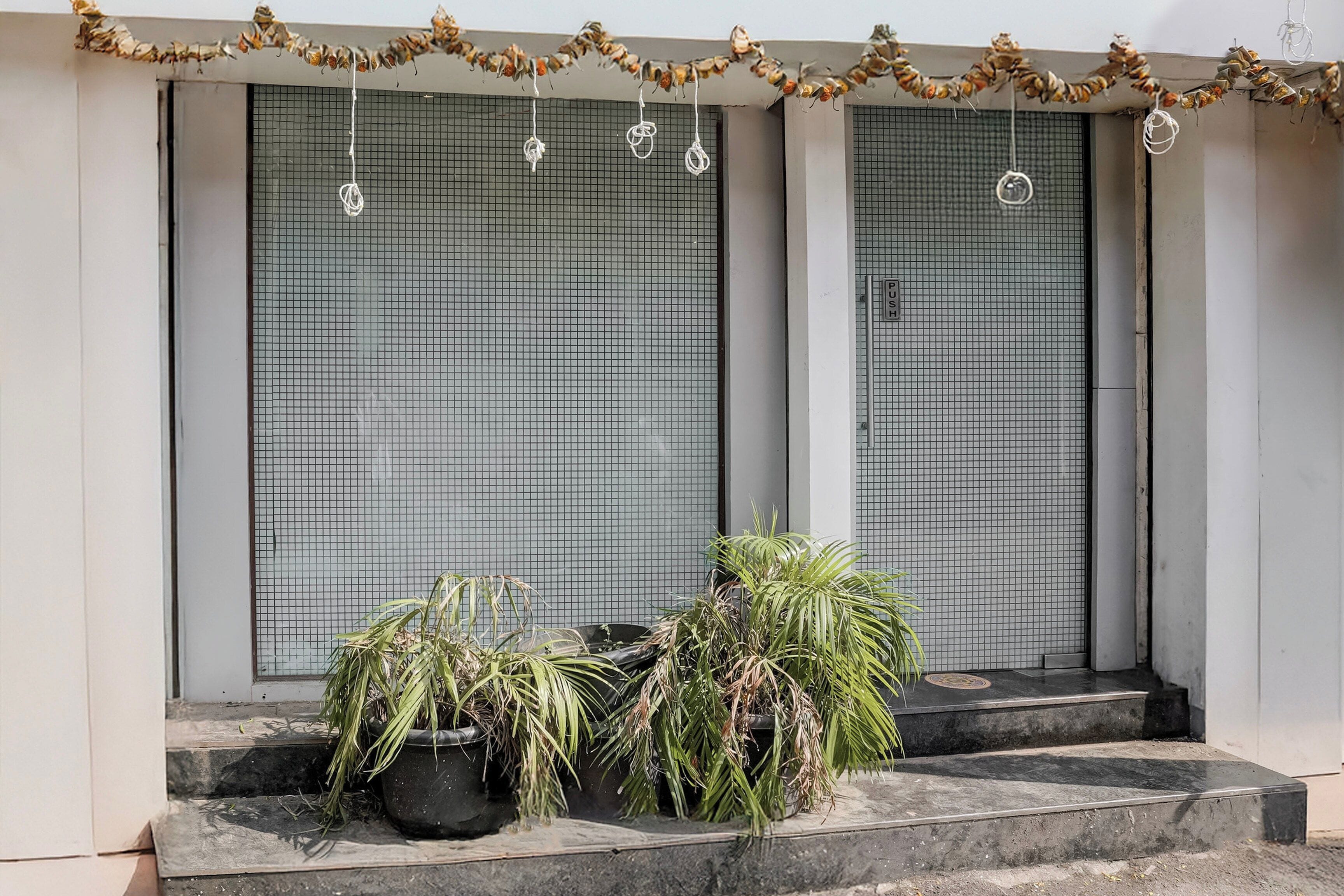 Una entrada de edificio con dos puertas cerradas, un escalón que conduce a la entrada y una guirnalda de flores secas sobre las puertas.