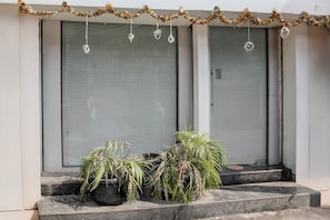 Una entrada de edificio con dos puertas cerradas, un escalón que conduce a la entrada y una guirnalda de flores secas sobre las puertas.