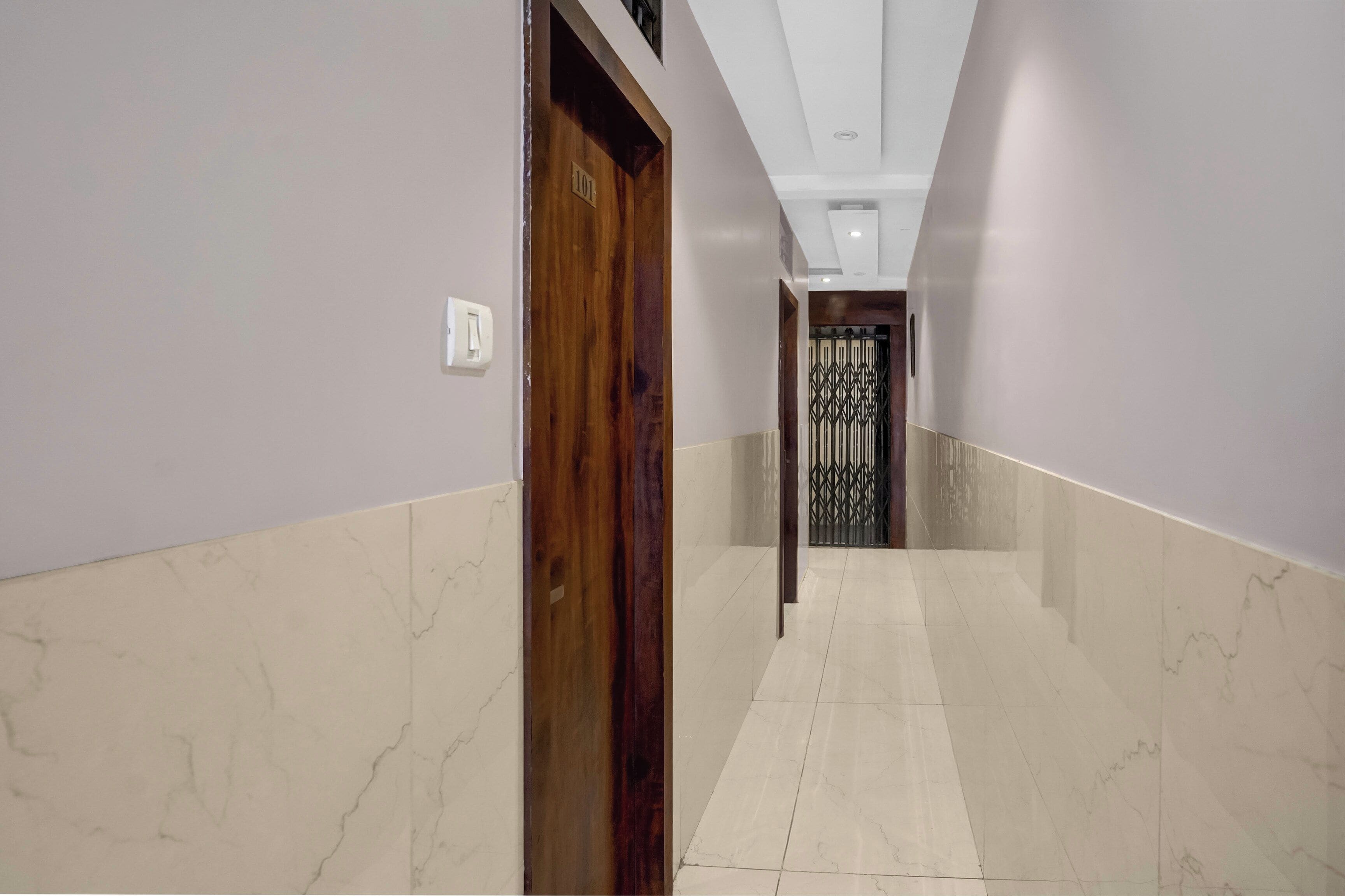 Un pasillo con una puerta de madera marcada '101' y una reja metálica al final.