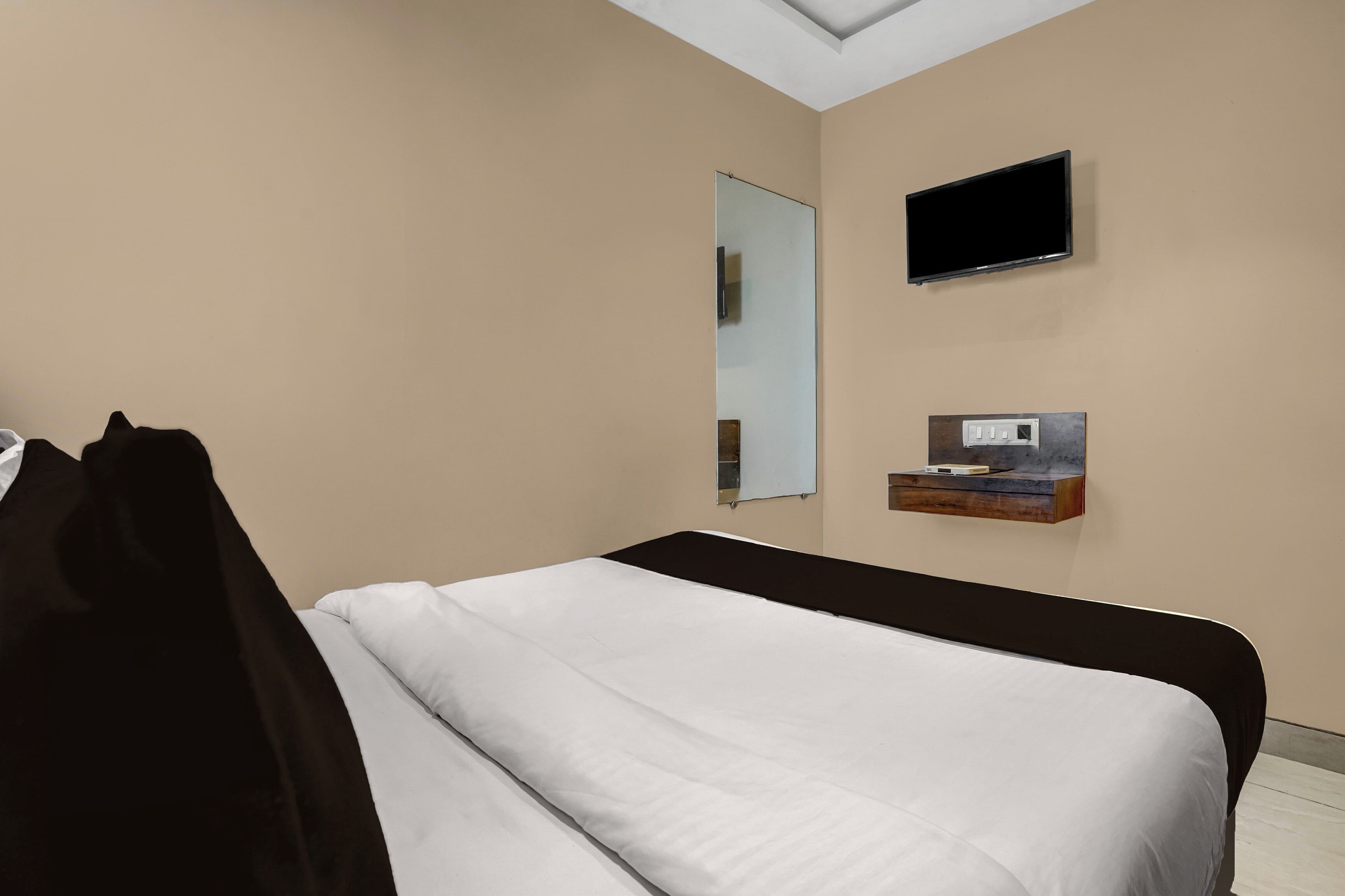 Un dormitorio con cama, televisor, espejo y una pequeña estantería con un calefactor.