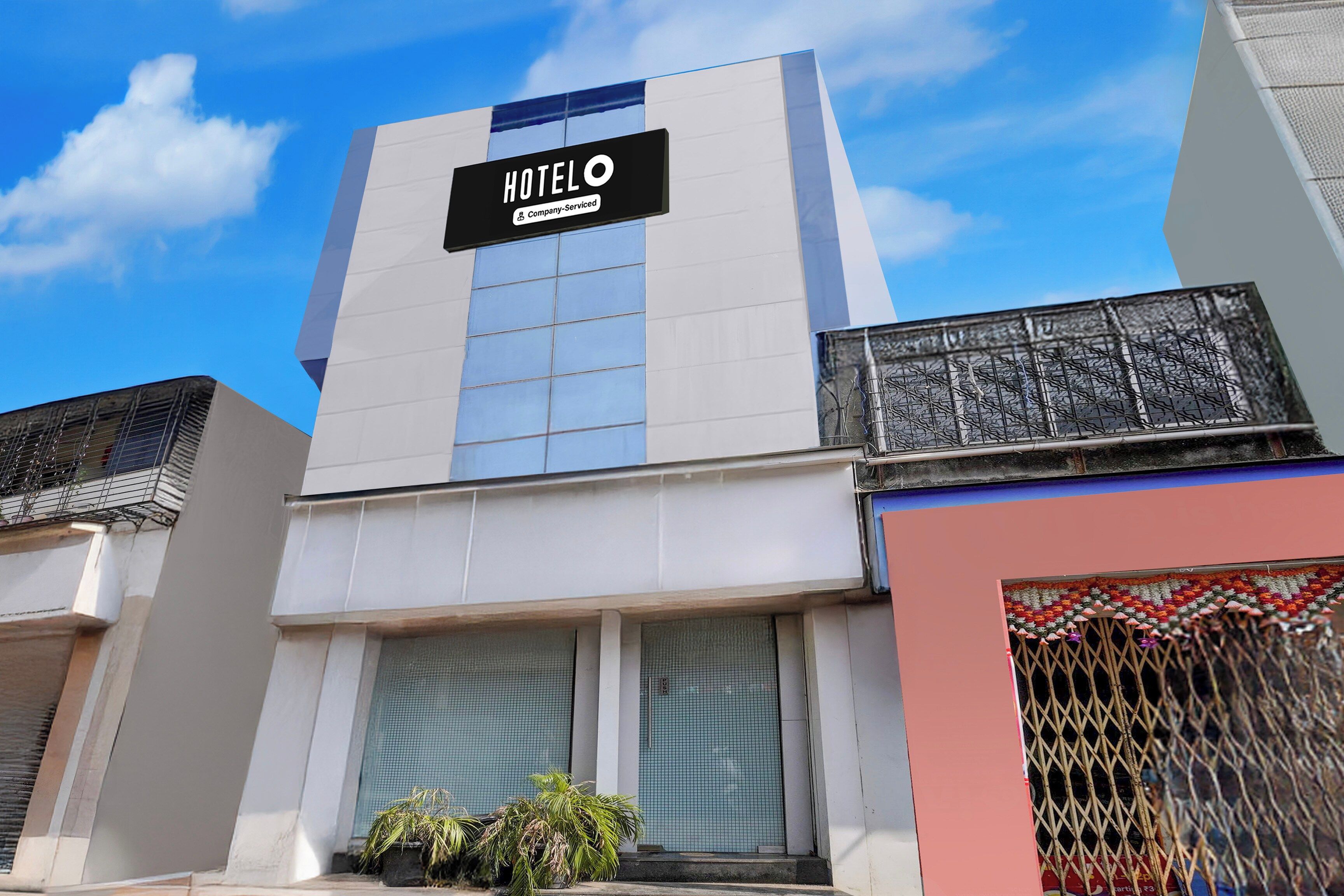 Un hotel llamado 'HOTELO' con un diseño moderno, que cuenta con un letrero destacado, ventanas amplias y un balcón con barandilla de metal.