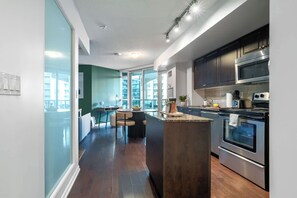 A modern kitchen with stainless steel appliances, a dining area with a round table, and a view through a glass wall. - Fort York 1BR, Balcony Near the Waterfront (Toronto)
