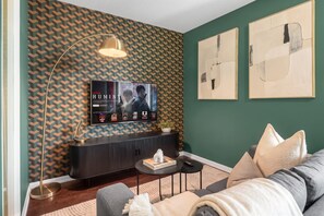 A living room with a flat-screen TV mounted on a patterned wall, a dark console table, a round coffee table, and a sofa with cushions. - Fort York 1BR, Balcony Near the Waterfront (Toronto)