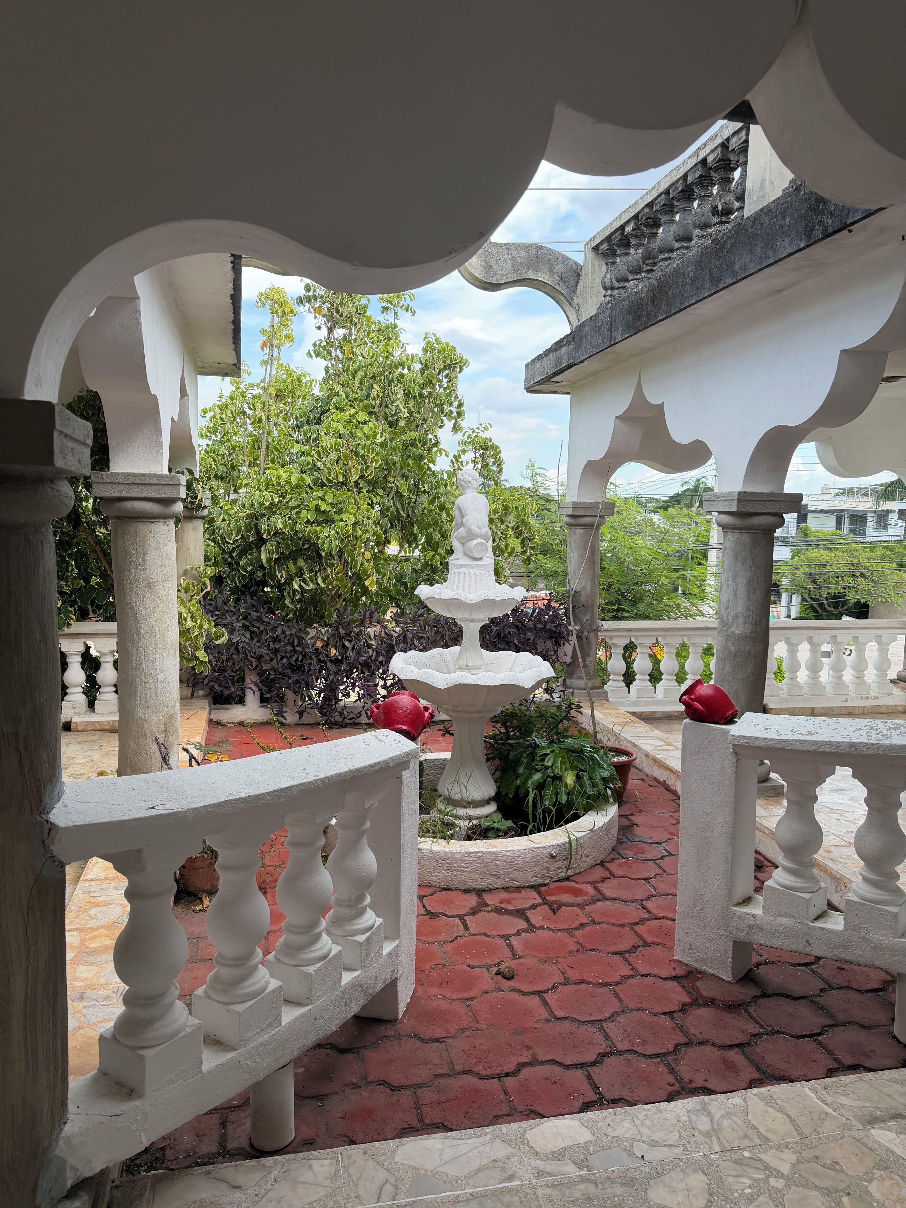 A courtyard with a fountain, potted plants, and a white balustrade.