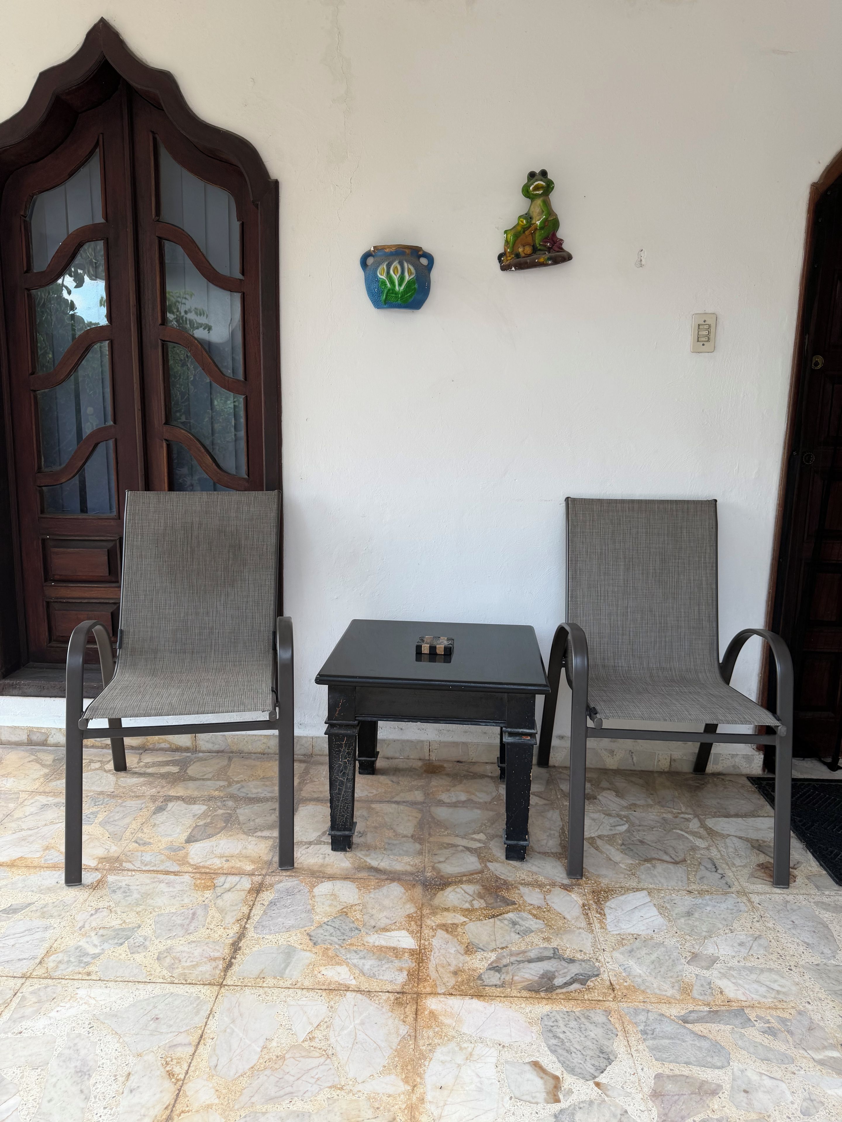 A patio with two chairs and a table, a wooden door, and a wall-mounted decorative plate.