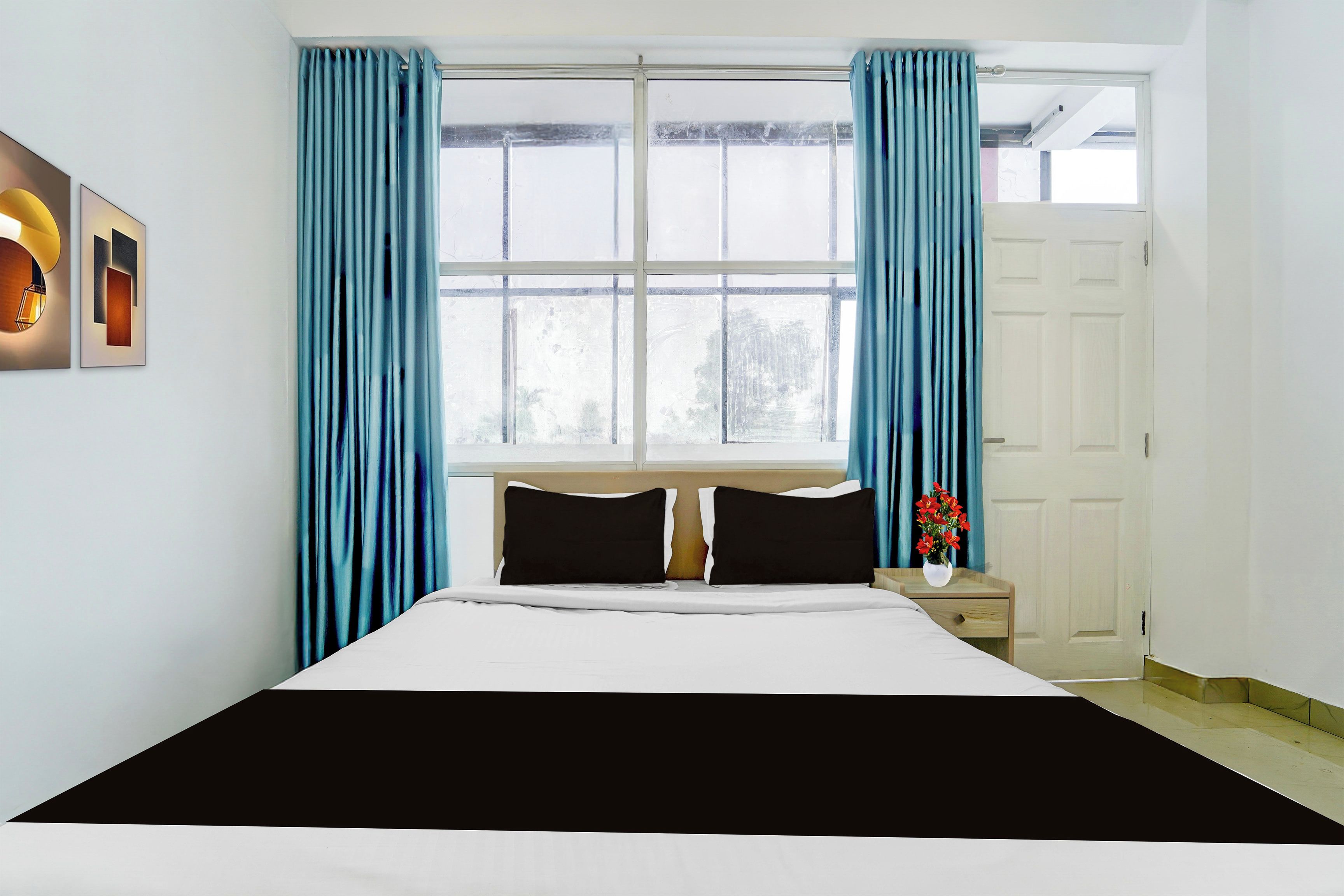 Un dormitorio con cama, mesita de noche, ventana con cortinas y puerta.