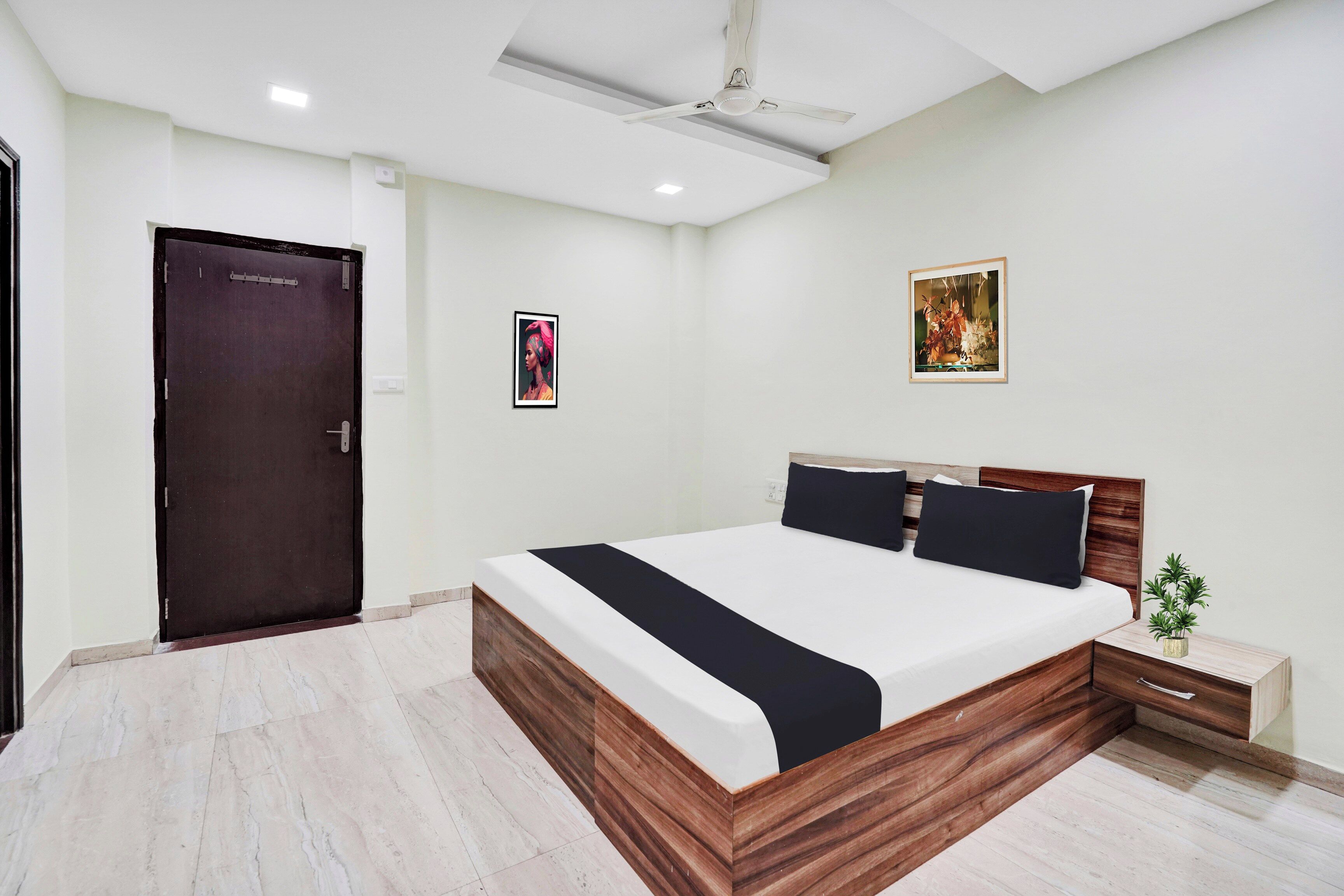 A modern bedroom with a wooden bed frame, a nightstand, a small potted plant, and a door.