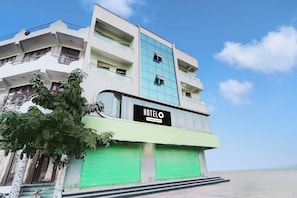 A multi-story hotel with a prominent 'HOTELO' sign, a green shuttered entrance, and a clear blue sky in the background.
