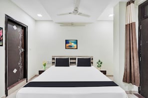 A hotel room with a bed, a ceiling fan, a painting, a nightstand, and a door.