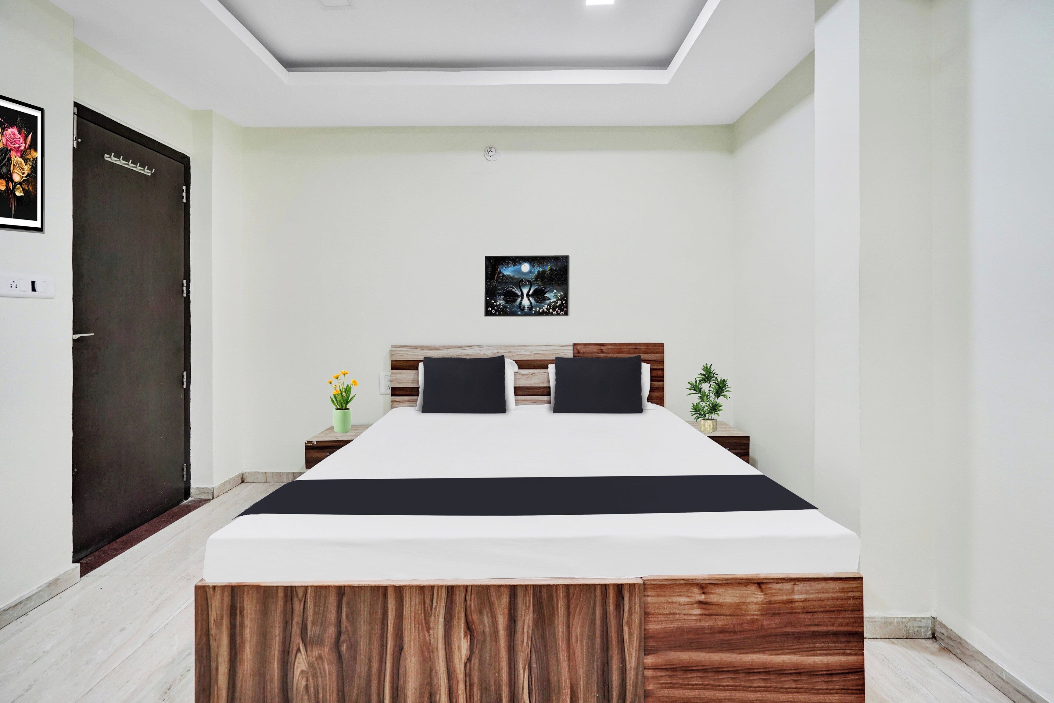 A bedroom with a bed, a nightstand, a potted plant, and a door.
