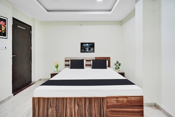 A bedroom with a bed, a nightstand, a potted plant, and a door.