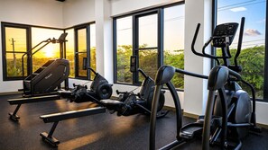 A gym with various exercise equipment, large windows, and a view of greenery. - Ground-Floor 1BR Retreat | Oversized Private Patio (Noord)