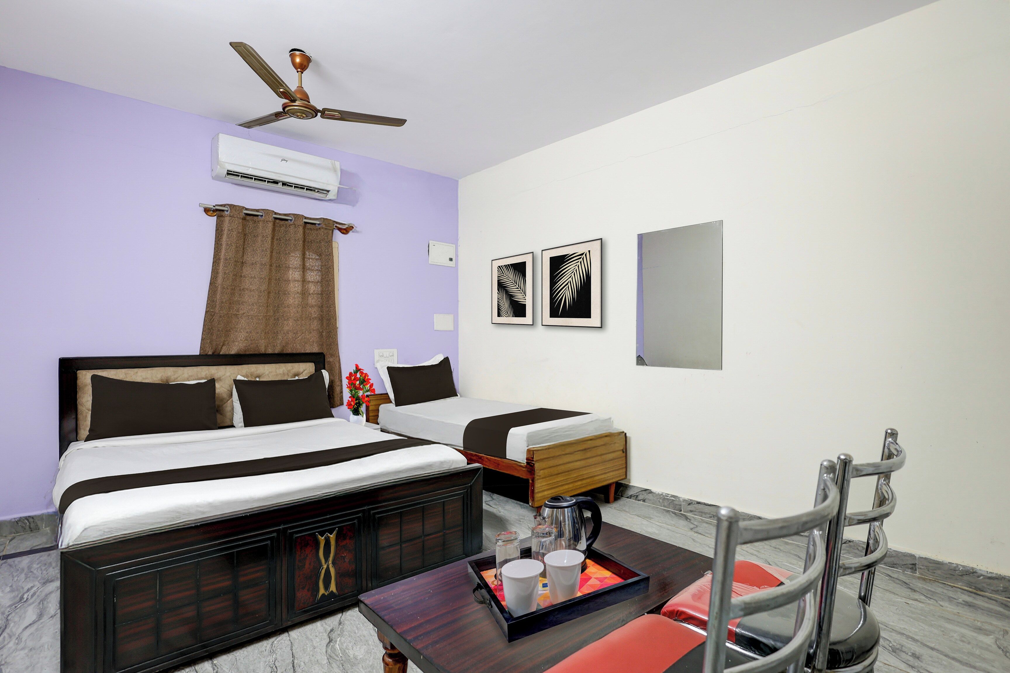 Quarto de hotel com cama, escrivaninha com bandeja de objetos, cadeira, ventilador de teto e arte nas paredes.