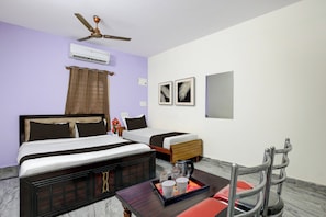 Habitación de hotel con cama, escritorio con bandeja de objetos, silla, ventilador de techo y obras de arte colgadas en la pared.
