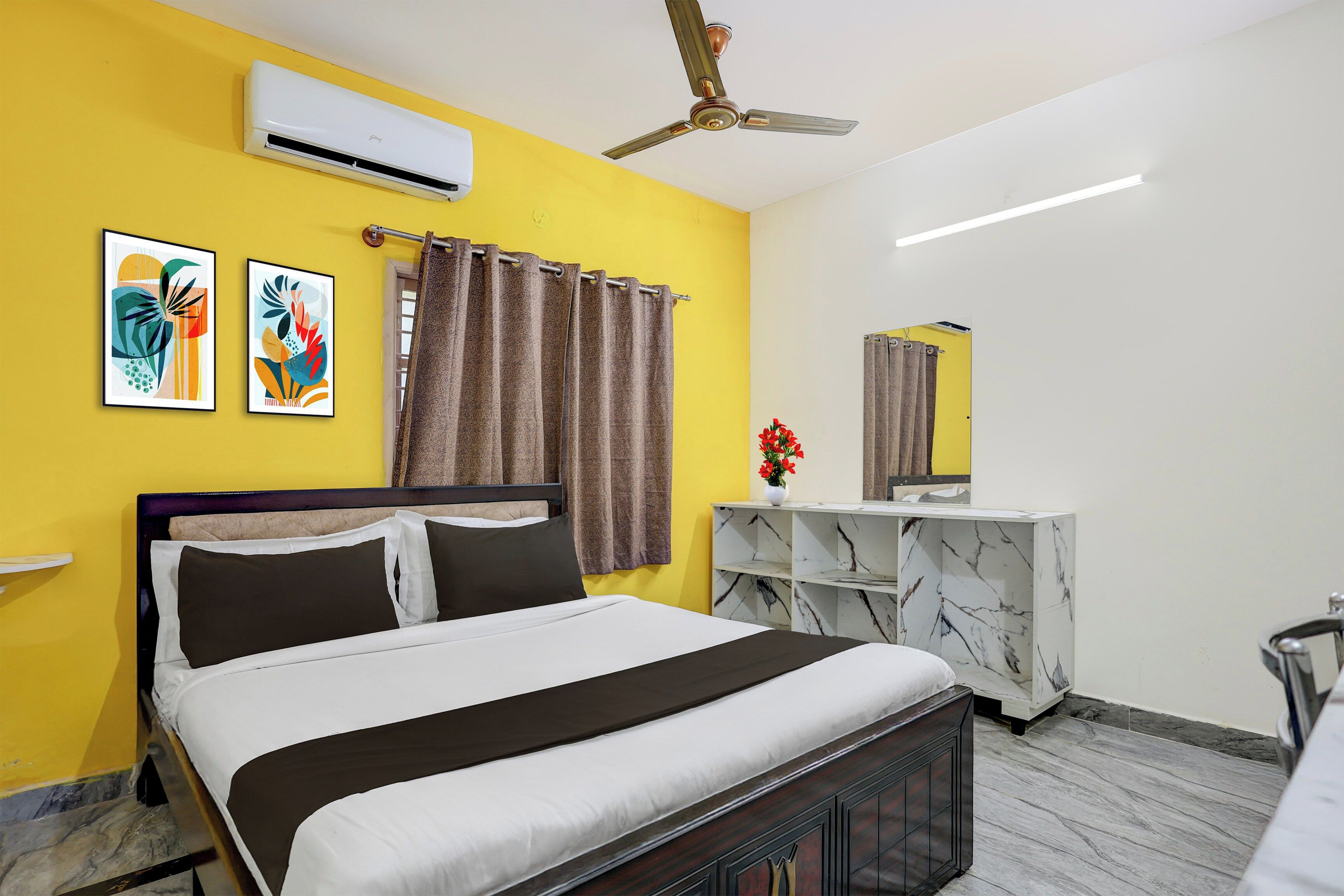 Une chambre d’hôtel comprenant un lit, un ventilateur de plafond, un appareil de climatisation, une console aux motifs imitant le marbre et un miroir.