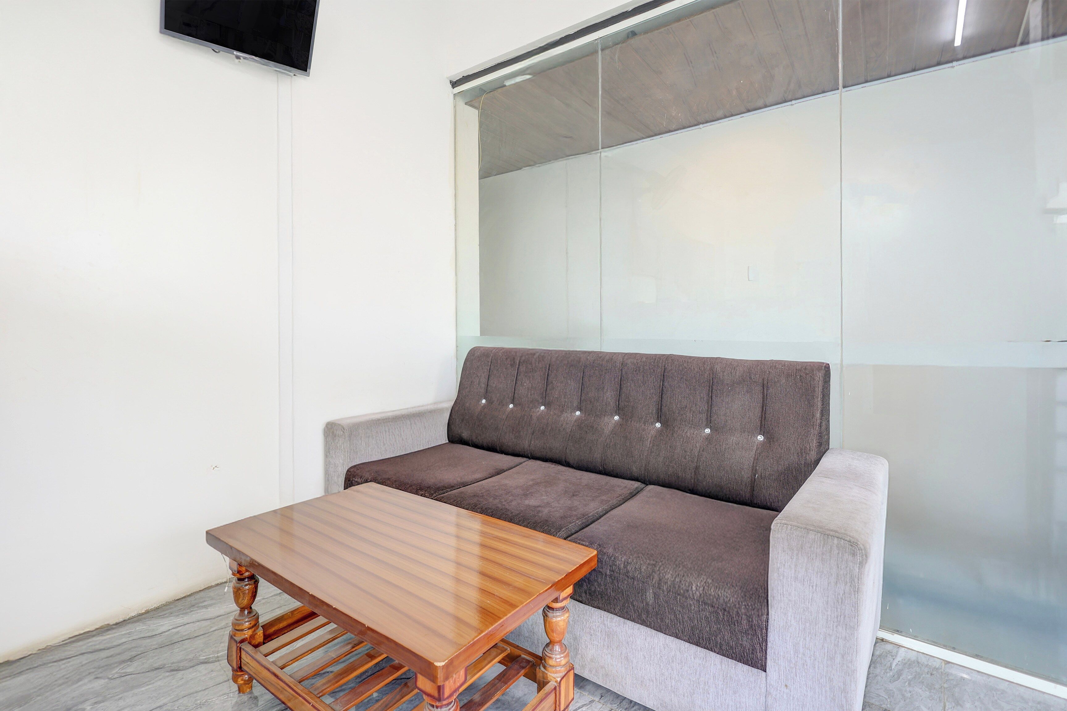 Una habitación moderna con un sofá gris, una mesa de centro de madera y un separador de vidrio.