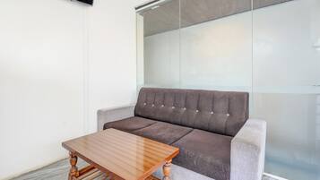 Una habitación moderna con un sofá gris, una mesa de centro de madera y un separador de vidrio.