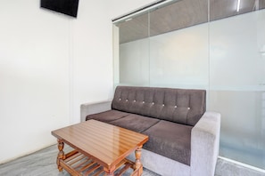 Una habitación moderna con un sofá gris, una mesa de centro de madera y un separador de vidrio.