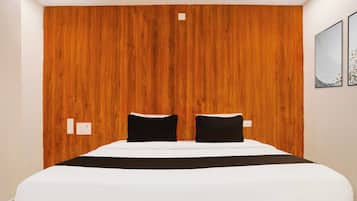 A hotel room with a wooden headboard, a bed with white bedding, two black pillows, and a single black throw blanket.