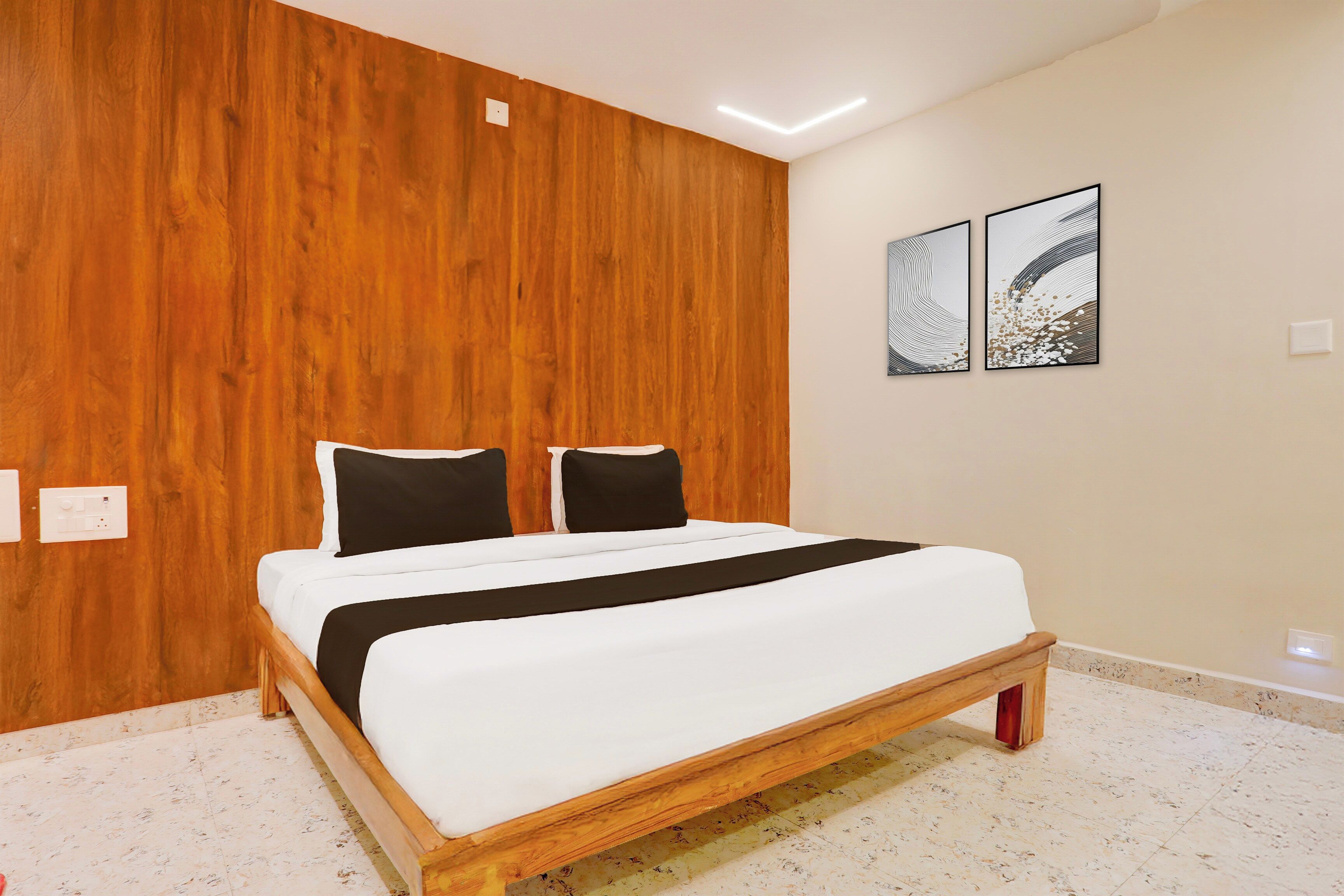 Un dormitorio con cabecera de madera, cama con ropa blanca y almohadas negras, y dos obras de arte abstracto en la pared.
