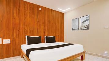 Un dormitorio con cabecera de madera, cama con ropa blanca y almohadas negras, y dos obras de arte abstracto en la pared.