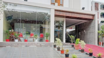 A modern building with a glass facade, outdoor seating area, and potted plants.