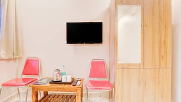 A room with a wooden cabinet, two red chairs, a small wooden table with a kettle, a remote control, and a water bottle.