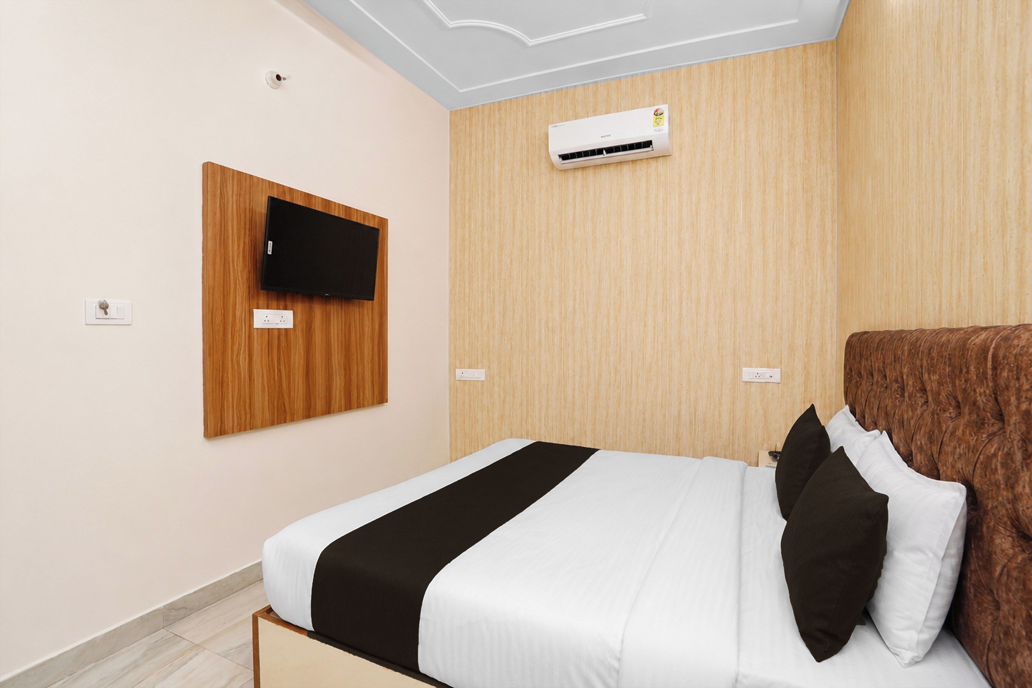 Una habitación de hotel con una cama, un televisor montado y un equipo de aire acondicionado.
