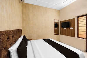 Habitación de hotel con una cama grande, cabecera de madera, televisor de pantalla plana montado en la pared y ventana con persianas horizontales.