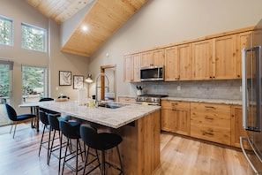 A modern kitchen with wooden cabinets, a granite countertop, and a stainless steel refrigerator. - Luxury Pines Retreat at Black Butte Ranch (Sisters)