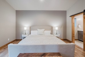 Une chambre à coucher avec un grand lit, deux tables de chevet avec des lampes, un plancher en bois et une porte en bois.