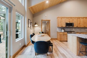 Une cuisine moderne avec des meubles en bois, un coin repas doté d’une table ronde et de chaises, et une grande fenêtre laissant entrer la lumière naturelle.
