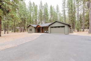 A two-story cabin with a garage, surrounded by tall pine trees. - Luxury Pines Retreat at Black Butte Ranch (Sisters)